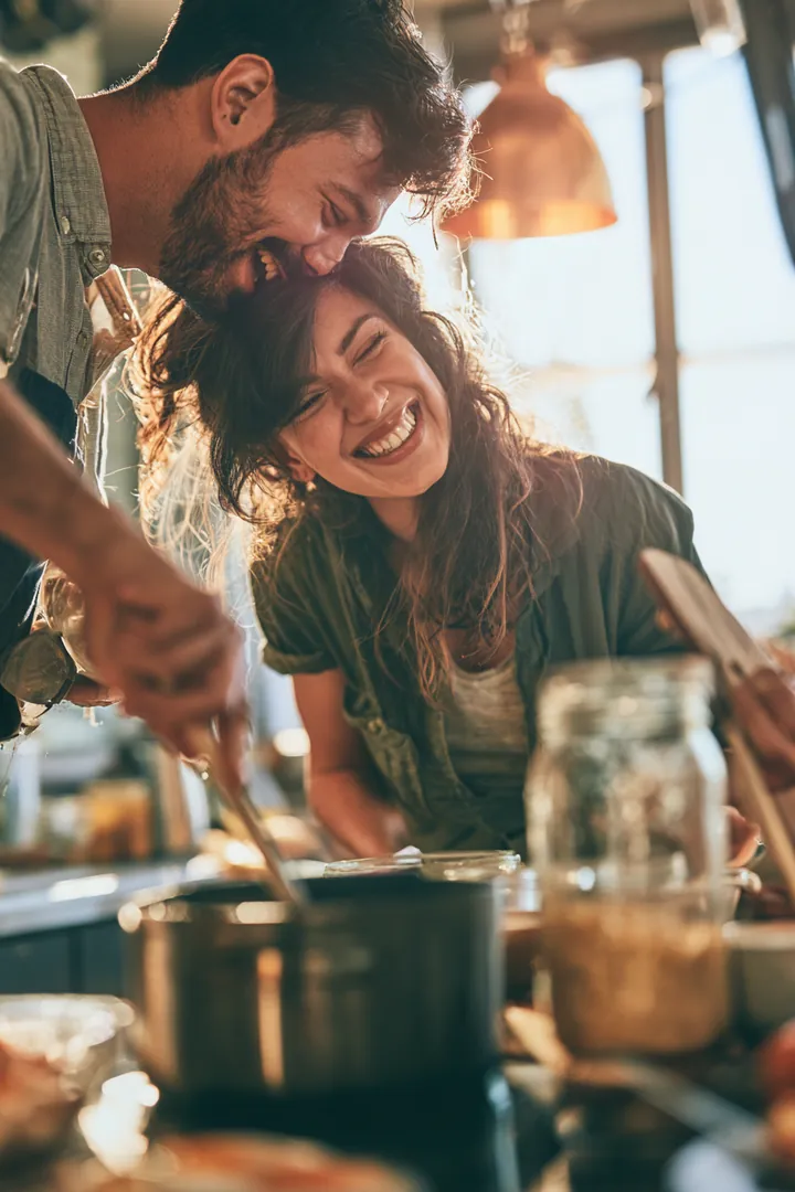 Couple in their 30s laughing while cooking breakfast together in a bright kitchen after finishing a loan instant cash request