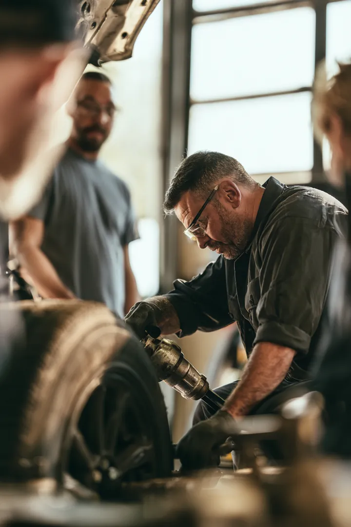 Over-the-shoulder view of a mechanic in his 40s tightening lug nuts with an impact wrench while the car owner watches, a repair covered by a loan instant cash request
