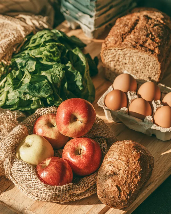 Weekly grocery haul on a light wood counter with apples, leafy greens, eggs and whole-grain bread, planned to fit a loan instant cash repayment budget