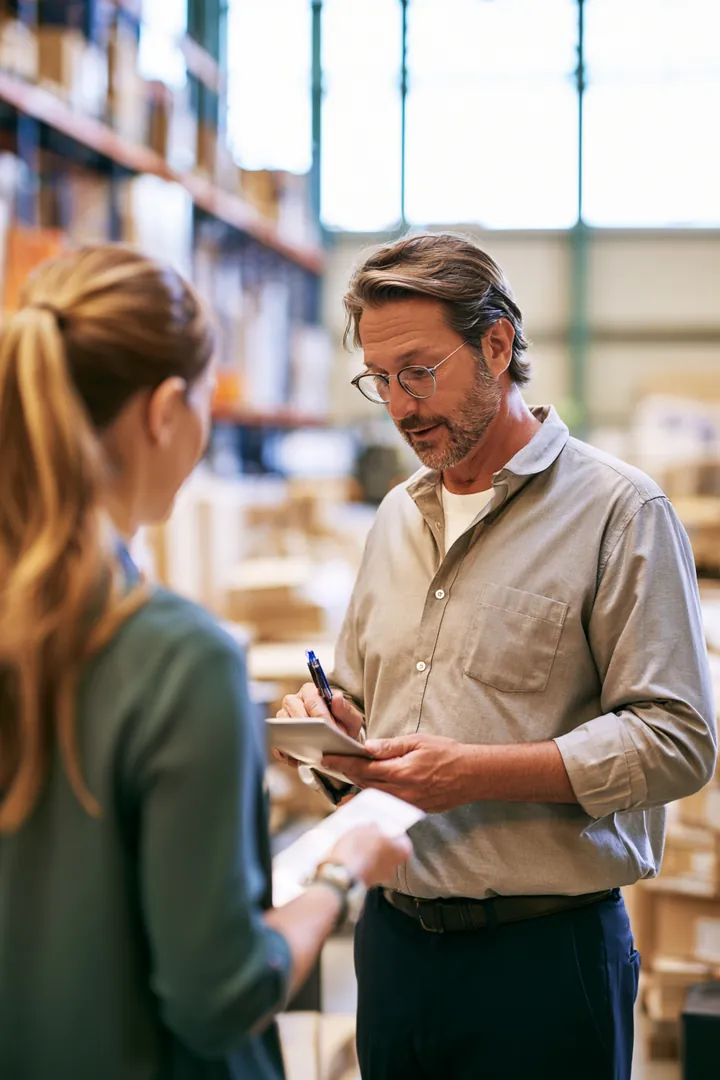 Shift lead in his 40s showing a new hire around a bright, organized distribution warehouse floor