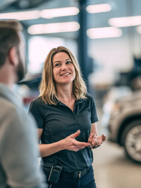 Service advisor in her forties guiding a customer through the service bay of a clean modern auto shop